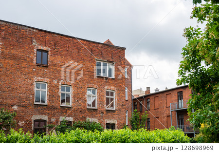 Old red brick residential buildings with overgrown garden and cloudy sky in Europe 128698969