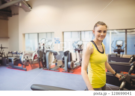 Standing woman using treadmill inside gym, with ellipticals and windows, copy space 128699041