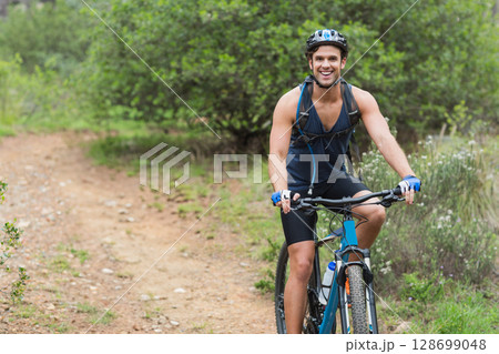 Pedaling man riding mountain bike on narrow trail in woods, with hydration pack, helmet, copy space 128699048