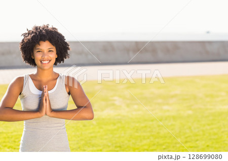 Practicing African American woman pressing hands together on waterfront lawn by seawall, copy space 128699080