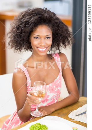 Smiling mid-adult African American woman holding wine glass at wooden dining table, with green peas 128699156