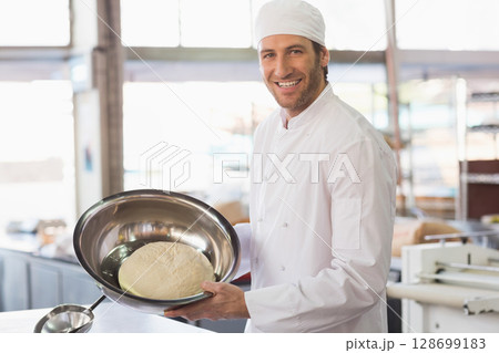 Holding dough in stainless steel bowl, male chef working at counter in bakery kitchen, copy space 128699183