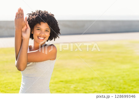 Stretching African American woman pressing palms on sunlit green field, fitness theme, copy space 128699346