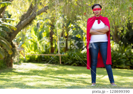 Posing woman in backyard wearing red superhero mask, cape, white t-shirt and blue jeans, copy space Posing woman in backyard wearing red superhero mask, cape, white t-shirt and blue jeans, copy space 128699390