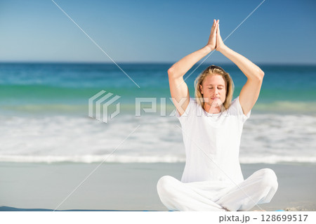 Meditating man raising hands above head on sandy beach shore with turquoise ocean, copy space Meditating man raising hands above head on sandy beach shore with turquoise ocean, copy space 128699517