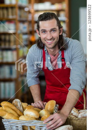 Smiling man leaning on counter in small bakery, with wicker baskets of fresh bread Smiling man leaning on counter in small bakery, with wicker baskets of fresh bread 128699522