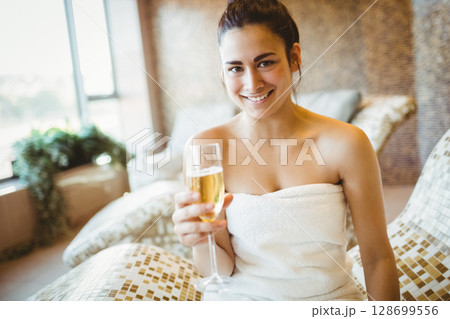 Relaxing woman holding champagne flute on mosaic chaise lounge in spa, with potted plant Relaxing woman holding champagne flute on mosaic chaise lounge in spa, with potted plant 128699556