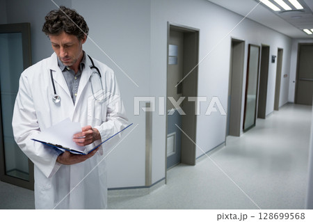 Reading male doctor reviewing chart in hospital hallway, with stethoscope and folder, copy space 128699568