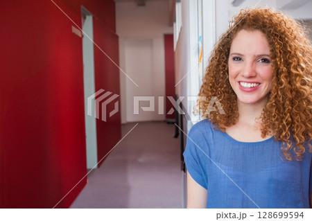 Leaning woman smiling in office corridor with red accent wall, bright sticky notes, copy space Leaning woman smiling in office corridor with red accent wall, bright sticky notes, copy space 128699594