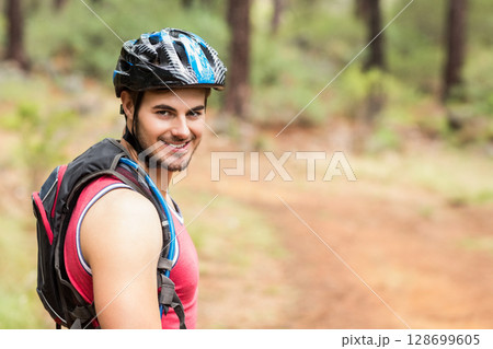 Smiling male cyclist turning head on pine forest trail, with helmet and backpack, copy space Smiling male cyclist turning head on pine forest trail, with helmet and backpack, copy space 128699605