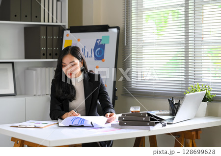 Businesswoman reviewing financial reports at her desk in a modern office with charts Businesswoman reviewing financial reports at her desk in a modern office with charts 128699628