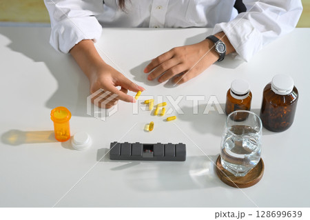 Daily supplement preparation with pill organizer, glass of water, and vitamin capsules Daily supplement preparation with pill organizer, glass of water, and vitamin capsules 128699639