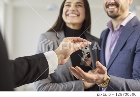 Young male realtor giving house key from new apartments to a happy smiling couple customers. 128700306
