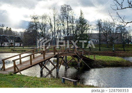 A small wooden bridge from the shore to a small island in the lake in the manor park A small wooden bridge from the shore to a small island in the lake in the manor park 128700353