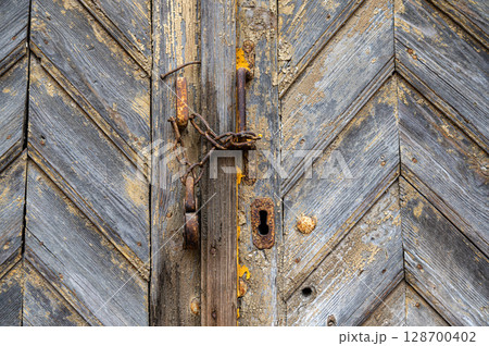 Rusty padlock locking old wooden door with a chain 128700402