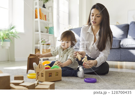 Caring mother playing with her little son, building wooden house, posing on warm floor in cozy room 128700435