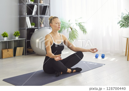 Portrait of a relaxed young woman doing yoga exercise at home sitting in lotus pose. Portrait of a relaxed young woman doing yoga exercise at home sitting in lotus pose. 128700440