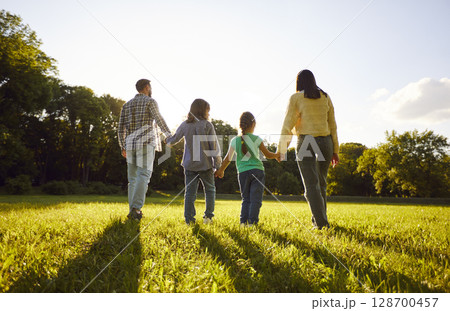 Back view of family of four with daughter and son walking outdoors enjoying beautiful nature. 128700457