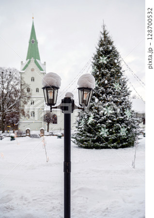 Snowy lantern with decorated Christmas tree and church in blurred background, shallow DOF Snowy lantern with decorated Christmas tree and church in blurred background, shallow DOF 128700532