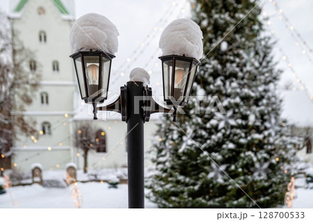 Snowy lantern with decorated Christmas tree and church in blurred background, shallow DOF Snowy lantern with decorated Christmas tree and church in blurred background, shallow DOF 128700533