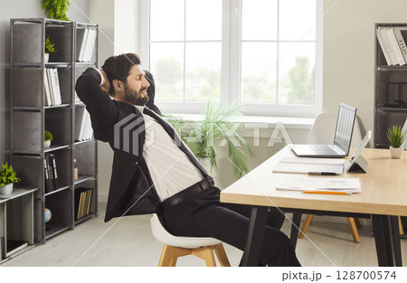 Young man employee in formal suit working on a laptop sitting at the desk in office. 128700574