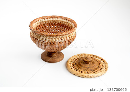 A wicker container with a lid on a wooden leg, isolated on a white background. Closeup. A wicker container with a lid on a wooden leg, isolated on a white background. Closeup. 128700666