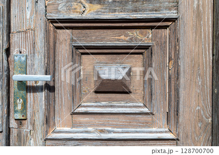 A close-up view of an intricately designed rustic wooden door with a unique handle and textures 128700700