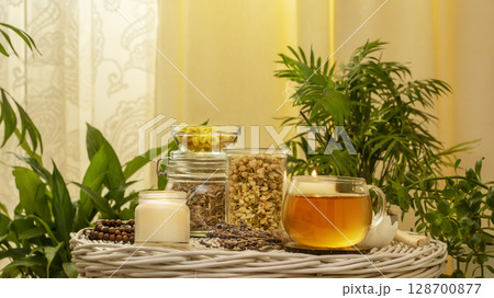 Home made herbal tea from wild plants and flowers. Home herbal apothecary concept. Healing and self care concept with natural dry flowers and herbs, cup of tea and candles in home interior with plants 128700877