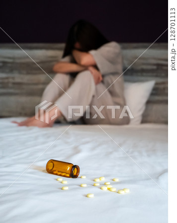 woman suffer from insomnia, focus on sleeping pills foreground on bed. front view of woman in stress in bedroom with sleep disorder. insomnia depression treatment concept woman suffer from insomnia, focus on sleeping pills foreground on bed. front view of woman in stress in bedroom with sleep disorder. insomnia depression treatment concept 128701113