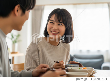 幸せな夫婦:リビングで夫と食卓を囲み、楽しく語り合う女性 幸せな夫婦:リビングで夫と食卓を囲み、楽しく語り合う女性 128701321