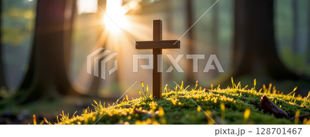 Handcrafted wooden cross stands on bed of moss, illuminated by sunlight filtering through trees, evoking serene atmosphere 128701467