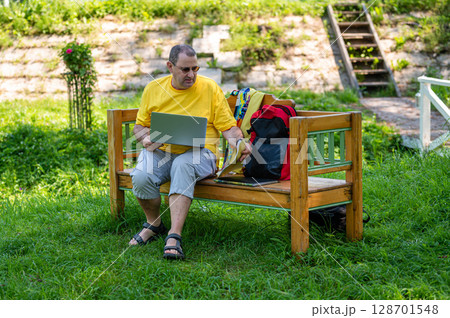 middle aged man with laptop and documents working outside in garden, green home office concept. middle aged man with laptop and documents working outside in garden, green home office concept. 128701548