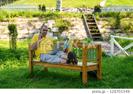 mature man with laptop and smartphone working outside in garden, green home office concept 128701549