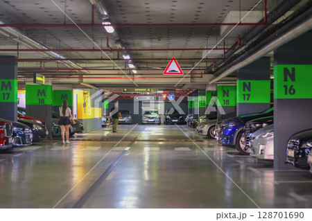 Rows of cars, Parking Garage. Modern underground parking with green section signs, visible directions, people walking past cars. Concept of urban transport Rows of cars, Parking Garage. Modern underground parking with green section signs, visible directions, people walking past cars. Concept of urban transport 128701690