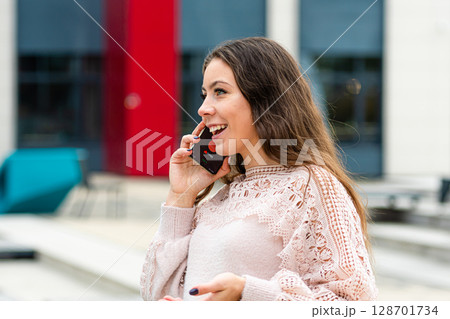 Young Woman Engaging in Cheerful Phone Conversation Outdoors on Bright Sunny Day Young Woman Engaging in Cheerful Phone Conversation Outdoors on Bright Sunny Day 128701734