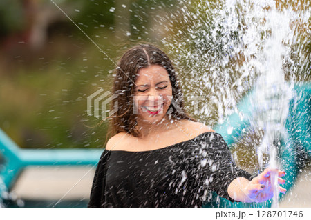 Joyful Woman Playing in Splashing Water at Outdoor Park in Bright Sunshine 128701746