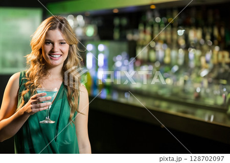 Woman in her 20s holding blue cocktail in martini glass at bar counter, smiling, copy space Woman in her 20s holding blue cocktail in martini glass at bar counter, smiling, copy space 128702097