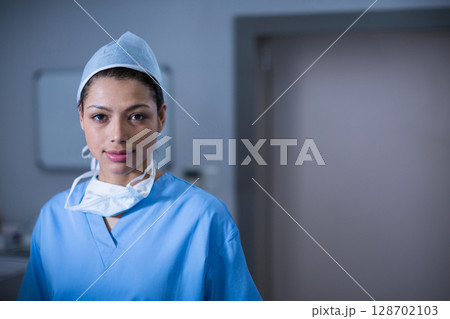 Female medical professional standing in prep room, wearing scrubs, cap and mask around neck Female medical professional standing in prep room, wearing scrubs, cap and mask around neck 128702103