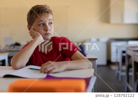 Gazing child resting cheek on hand at classroom desk, with notebook and pencil, copy space Gazing child resting cheek on hand at classroom desk, with notebook and pencil, copy space 128702122