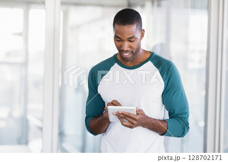 Tapping mid adult African American man using tablet in modern office corridor with glass partitions 128702171