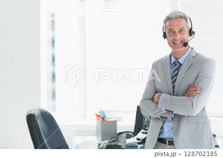 Smiling man standing in corporate office wearing headset with monitor and keyboard, copy space Smiling man standing in corporate office wearing headset with monitor and keyboard, copy space 128702185