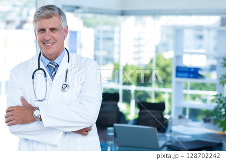 Standing male doctor wearing lab coat and stethoscope in medical office with laptop, copy space 128702242