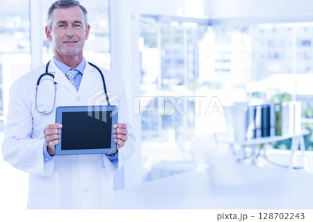 Male doctor holding blank tablet in medical office, showing stethoscope and files Male doctor holding blank tablet in medical office, showing stethoscope and files 128702243