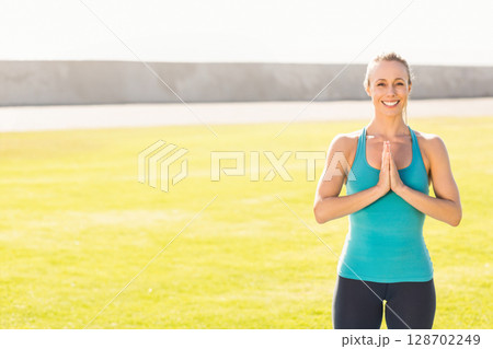 Woman holding prayer pose and smiling in wide grassy field under bright sky, copy space Woman holding prayer pose and smiling in wide grassy field under bright sky, copy space 128702249