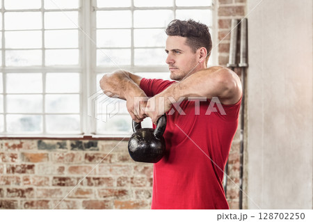 Man lifting kettlebell and working out at fitness studio, with large windows and weight plates Man lifting kettlebell and working out at fitness studio, with large windows and weight plates 128702250