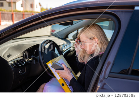 middle aged blonde business woman in glasses in car working with documents, mobile technology concept 128702588