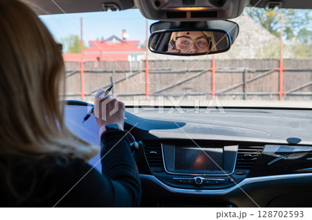 business woman working in the car and talking on the phone, face reflection in the rearview mirror 128702593
