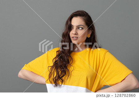 portrait of a young teenager with long wavy hair dressed in a yellow t-shirt, isolated on gray background 128702860