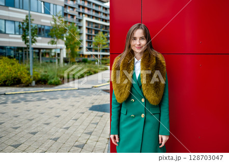 portrait of a woman at the red wall of a modern office building on a cool autumn day 128703047