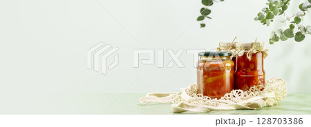 Probiotic food banner. Eco friendly still life with pickled or fermented vegetables in glass jars on textile bag on blue background with leaves and shadows. Home food preserving or canning. Copy space Probiotic food banner. Eco friendly still life with pickled or fermented vegetables in glass jars on textile bag on blue background with leaves and shadows. Home food preserving or canning. Copy space 128703386
